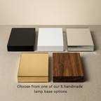 The five Lumo Bloc lamp base finishes: Black Paint, White Paint, Silver Mirror, Gold Mirror, and Sealed Woodgrain (Walnut) — choose from one of our 5 handmade lamp base options